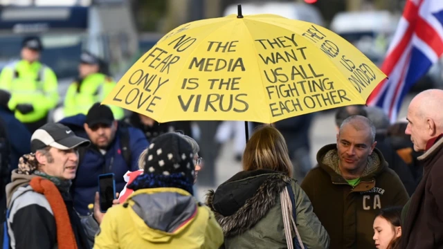 Anti-vaccine protest in London, UK. Small group under yellow umbrella with "media is the virus" slogan