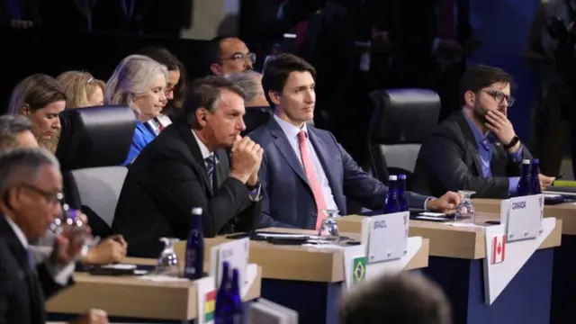 O presidente Bolsonaro ao lado do primeiro-ministro do Canadá, Justin Trudeau, sentados na plateia e com outras pessoasjogar casino online gratisvolta