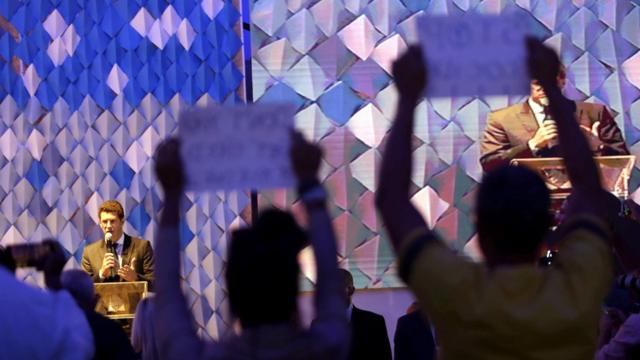 No planocodigo de bônus f12 betfundo, o ministro Ricardo Salles aparece falando no microfone; na plateia, duas pessoas levantam cartazescodigo de bônus f12 betprotesto