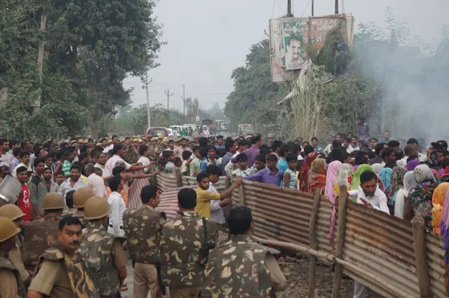 অনেক মানুষের ভিড়, একপাশে আইনশৃঙ্খলা বাহিনীর সদস্যরা, অন্যপাশে ধোঁয়া দেখা যাচ্ছে