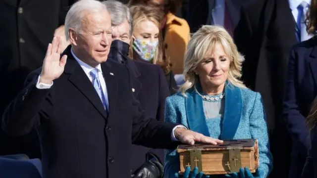Joe Biden take im oath with one had on di Bible