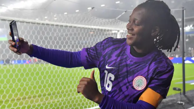 Nigeria goalkeeper Chiamaka Nnadozie stands behind a goal and takes a selfie giving a thumbs up after a football match