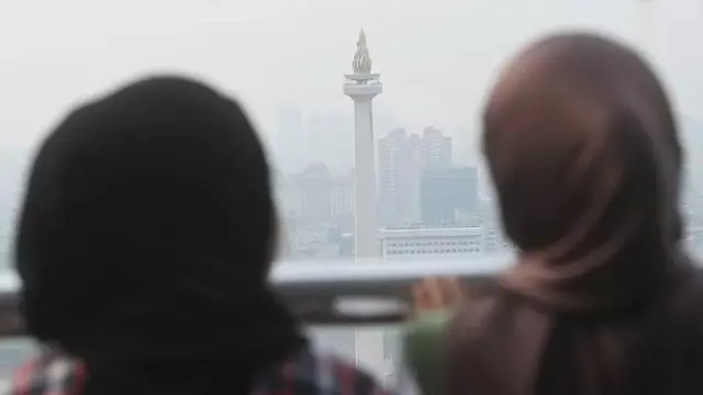 Dua wanita melihat tugu Monas yang tertutup oleh kabut polusi di Jakarta, Selasa (25/7/2023).