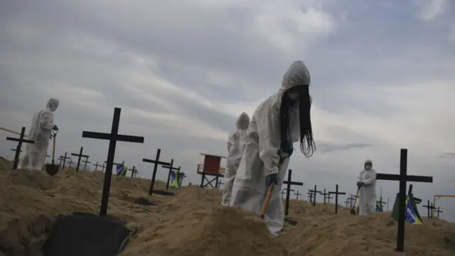 विरोधीहरूले भाइरसले निम्त्याएका मृत्युको सङ्केत गर्नेगरि एक समुद्री किनारमा साङ्केतिक रूपमा सुरक्षित कपडा लगाएर चिहान खनेका छन्