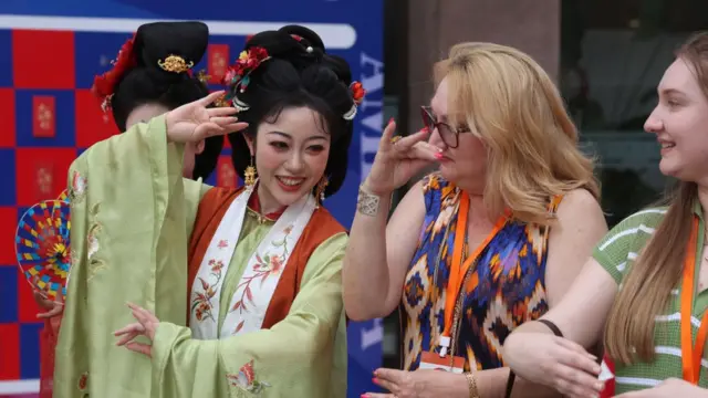 2024年6月12日，中国北京，一名身着中国传统服装的中国女性在中美青少年友谊主题音乐会前向美国友人展示中国传统礼仪。