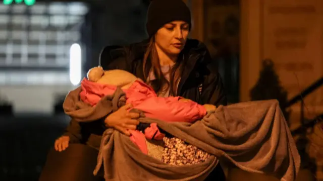 Жінка тримає на руках маленьку дитину, загорнуту в ковдру, вона йде вночі