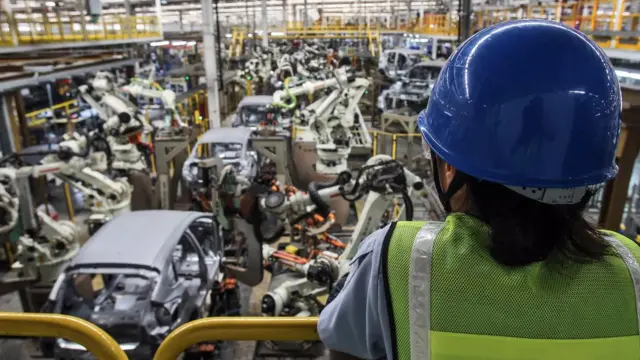 คนงานหญิงมองดูเครื่องจักรทำงานในโรงงานรถยนต์ ที่จ.ระยอง