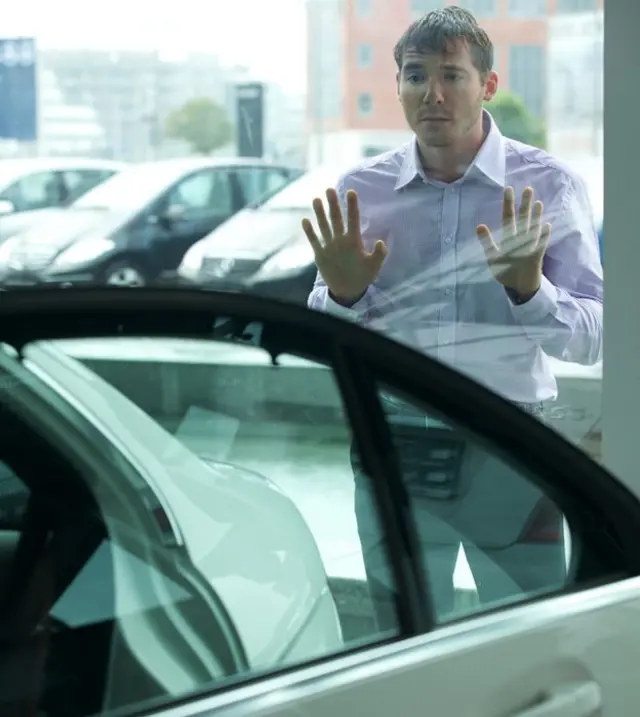 Hombre mirando por la ventana de un concesionario
