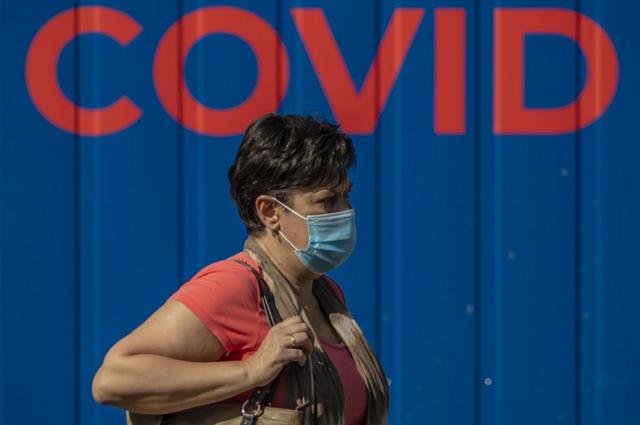 A woman wearing protective face mask walks in front of a coronavirus testing station