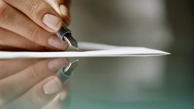 Una mano sostiene una pluma sobre un papel