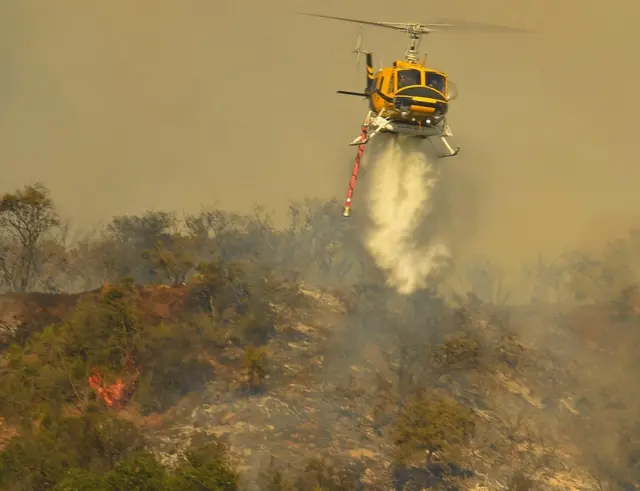 Helicóptero rociando agua sobre incendio