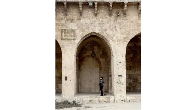 Seorang warga melakukan salat di Masjid Umayyah yang porak poranda.