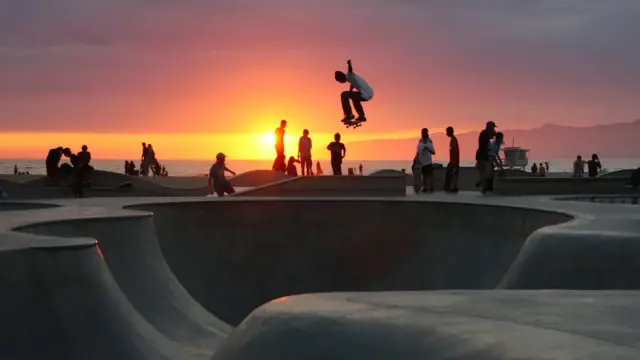 Pessoas andando de skate com pôr do Sol ao fundo