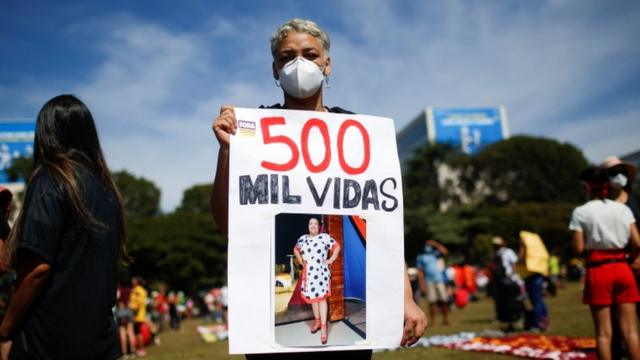 Mulher de máscara segura cartaz que diz '500 mil vidas' e expõe foto de uma mulher