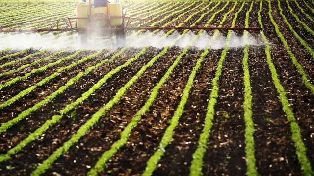 Un tractor con difusores de pesticidas arando un campo de cultivo.