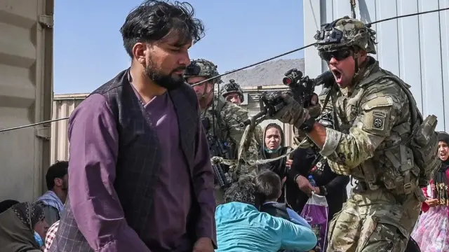 Un soldado estadounidense trata de controlar a los cientos de personas que desesperadas buscan subirse a un avión.