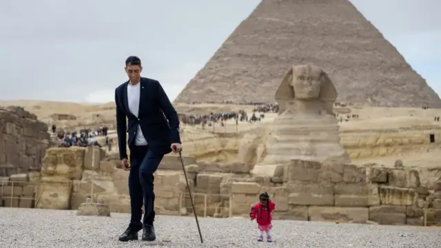 India's Jyoti Amge (R), the world's shortest woman poses for a picture with Sultan Kosen of Turkey, the world's tallest man, at the site of the Pyramids of Giza in Egypt on January 26, 2018, with the Sphinx and the Pyramid of Khafre (also known as Chephren) seen in the background