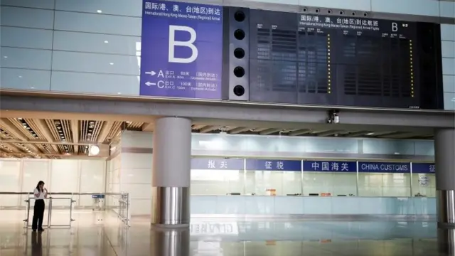 A woman uses a mobile phone near an information display for international flights and flights from Hong Kong, Macau and Taiwan, at Beijing Capital International Airport