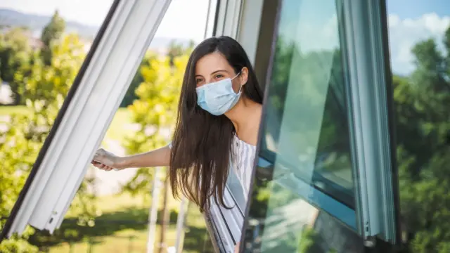 Mujer con una mascarilla abriendo una ventana