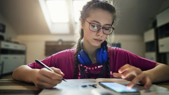 Menina mexe no celular enquanto estuda