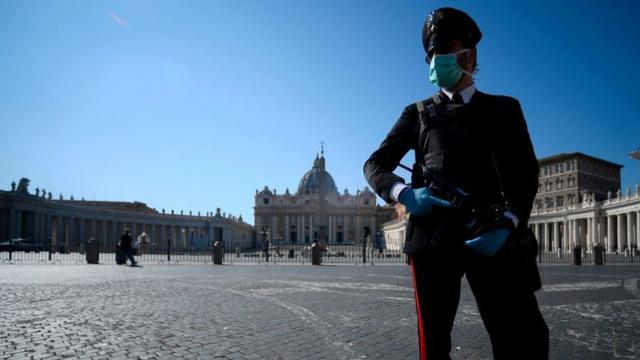 An armed police officer, wearing a face mask, patrols a closed and deserted St Peter's Square in the Vatican