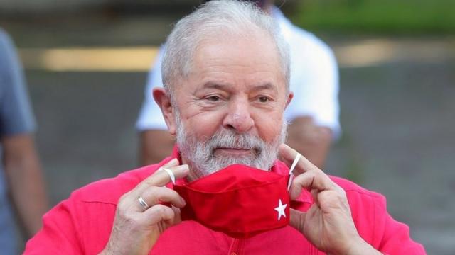 Lula tirando máscara contra a covid vermelha, com símbolo do PT