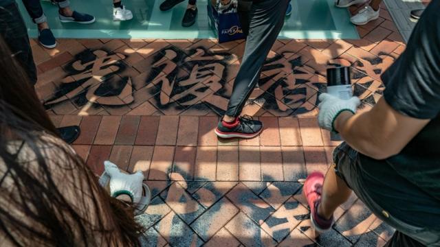 Students protesters walk over a graffiti slogan on the ground as they take part in the Occupy University Street rally