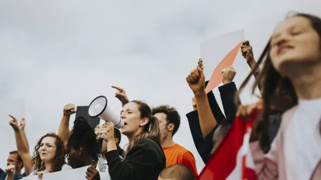 Jovens ao ar livre protestando com megafones e cartazes