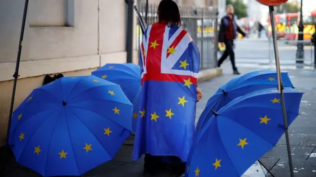 Une femme avec le drapeau, britannique sur le dos, entourée de parapluies aux drapeaux de l'UE