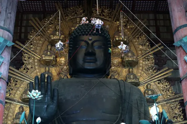 The Great Buddha of Nara at Todaiji Temple is cleaned by monks on pulleys.