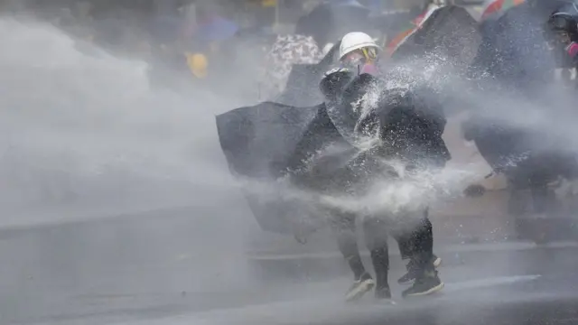 有示威者用雨伞抵挡水炮车的水柱。