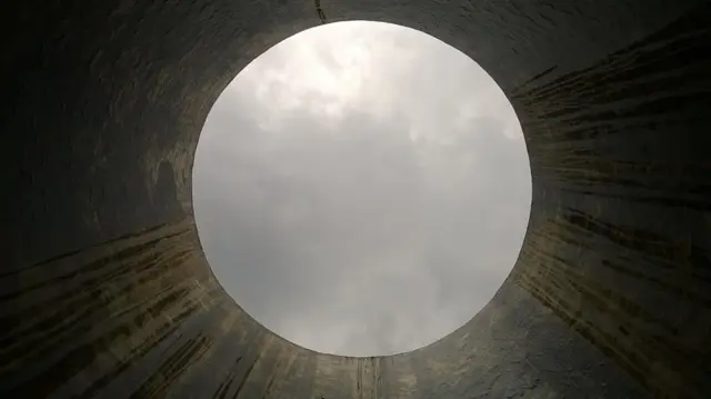 Interior de una torre con paredes húmedas, viendo hacia el cielo