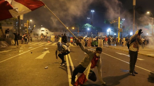 Foto noturna mostra manifestante com bandeira do Peru caindo no asfalto