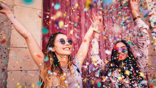 Cheerful female teenage best friends partying by throwing confetti in city streets