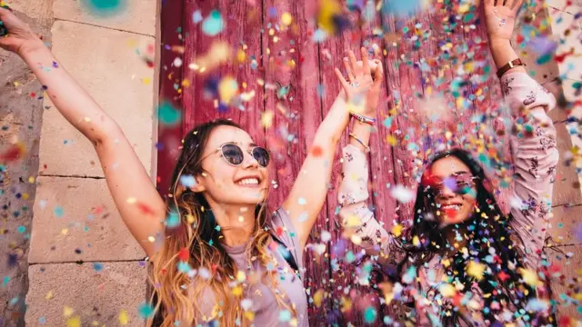 Cheerful female teenage best friends partying by throwing confetti in city streets