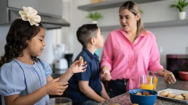 Una madre y sus dos hijos preparando el desayuno.