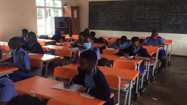 Muri iri shuri ryigenga umwana umwe ari ku ntebe ye, bicaye mu ishuri bambaye udupfukamunwa