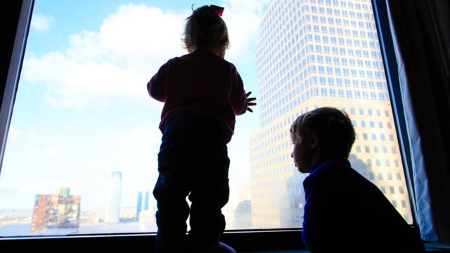 Duas crianças olhando cidade da janela de um apartamento