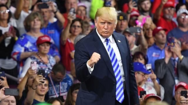 Trump aparece comemorando com um gesto, observado por dezenas de apoiadores na plateia