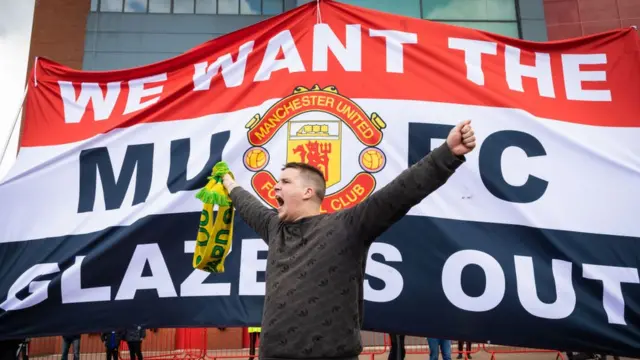 Болельщик на фоне транспаранта: "Мы хотим футбольный клуб "Манчестер Юнайтед", Глейзеры - вон!"