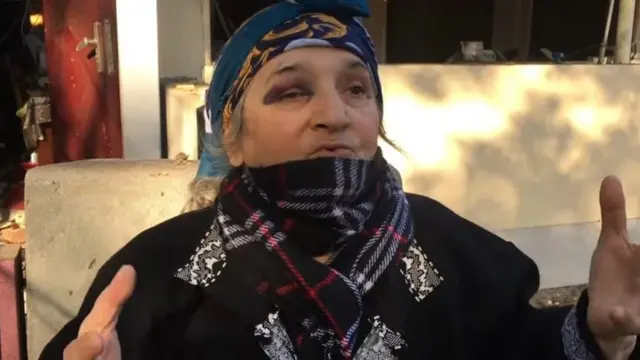 Пожилая жнщина в шарфе и косынке.