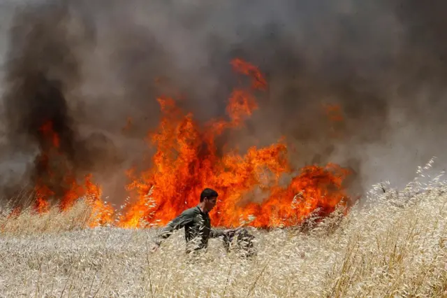 Un soldado israelí intenta apagar un incendio en un cultivo de trigo