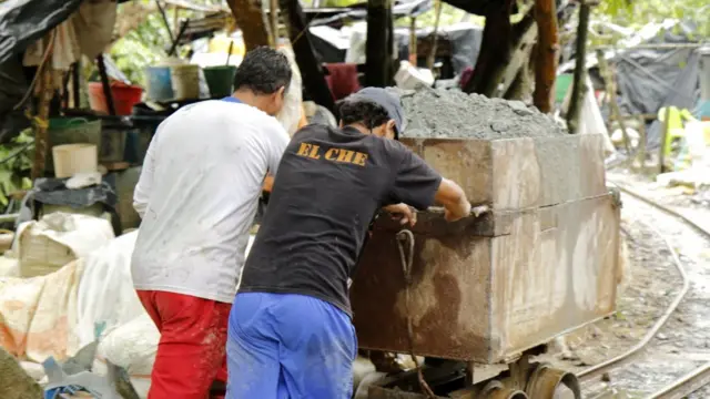Dos hombres empujan un carro con material de mina.