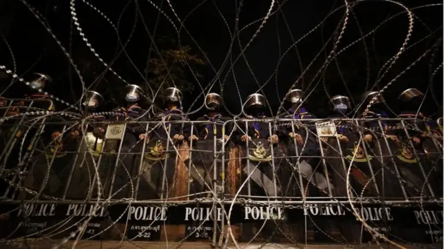 Riot police stand guard behind barbed wire road block during an anti-government protest in Bangkok, Thailand, 21 October 2020.