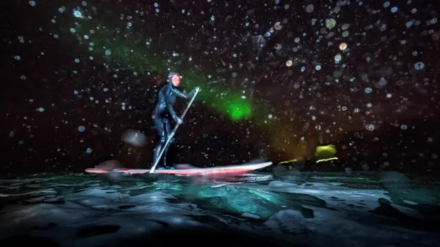 Женщина стоит на сапсёрфе ночью