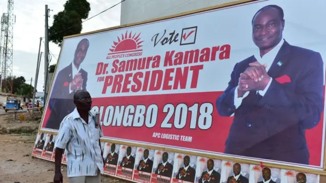 One man dey waka pass signboard of candidate Samura Kamara