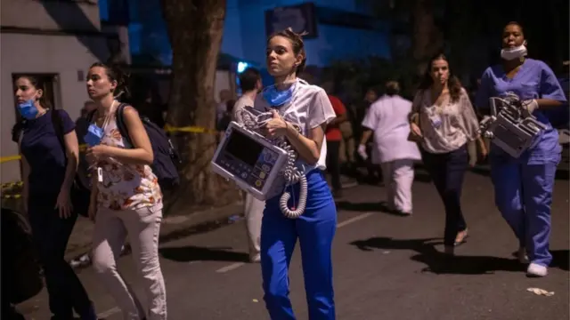 Profissionais de saúde carregam equipamentos para fora do hospital
