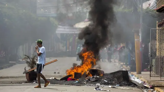 Hombre caminando cerca de una barricada en llamas.