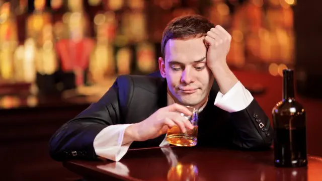 Un hombre tomando con desánimo en un bar.