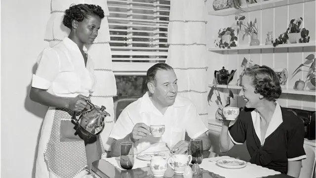 Black maid serves coffee to white couple